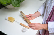 Hands holding the CaliWoods Cleaner Brush pack containing two natural straw pipe cleaners and Bottle Brush next to it on a kitchen bench.