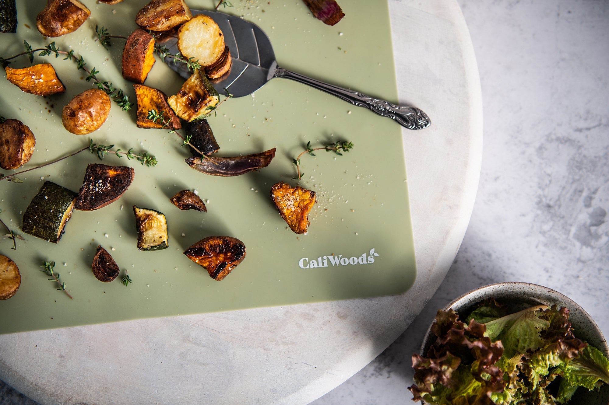 Roast vegetables with salt and thyme on a kitchen bench with a green Reusable Baking Mat