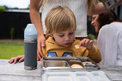 Pura kiki water bottle next to a boy with a stainless lunchbox sitting on a bench