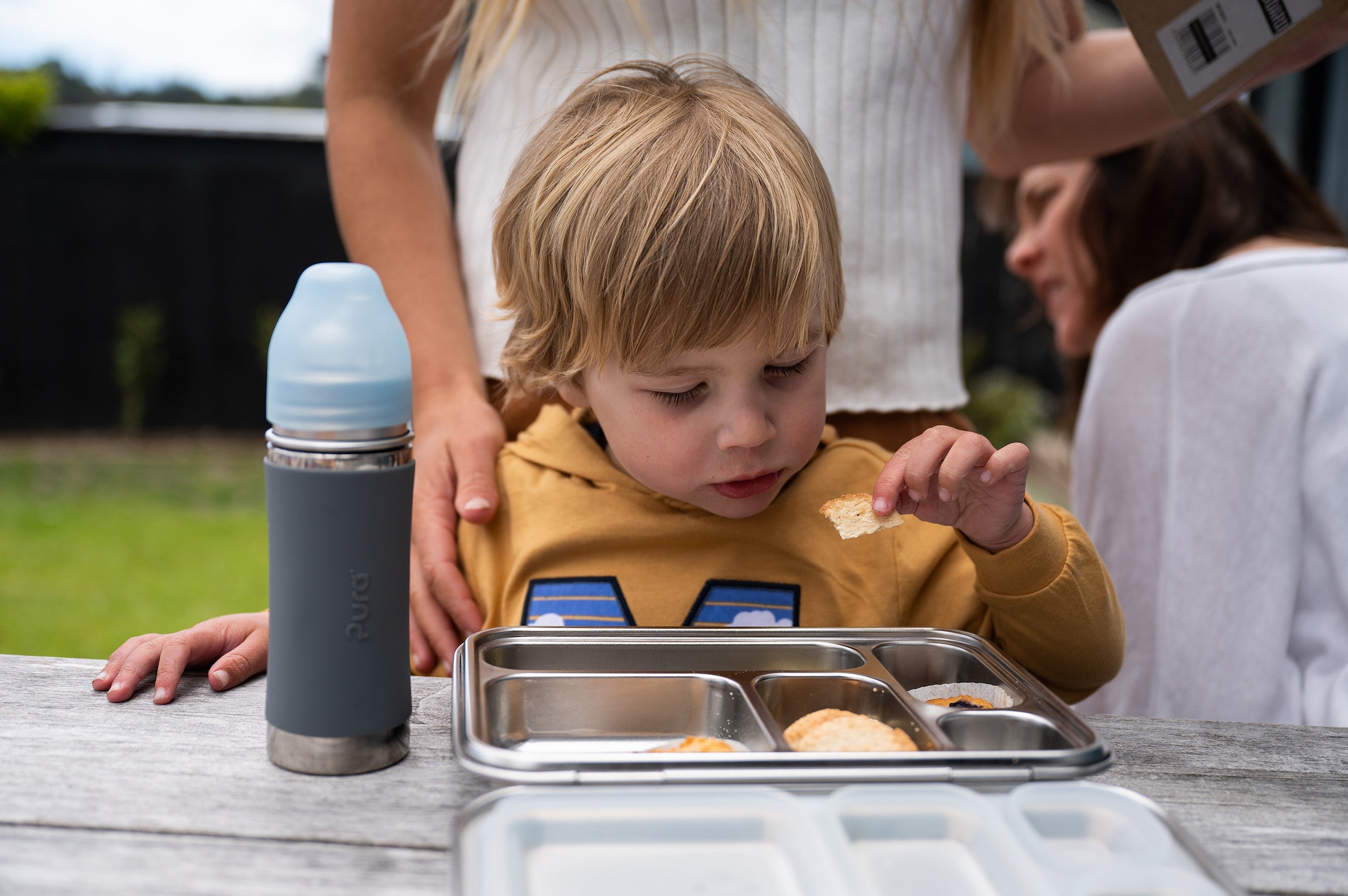 Pura kiki water bottle next to a boy with a stainless lunchbox sitting on a bench