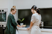 Two women smiling over a cake baked on a circular reusable cake tin liner