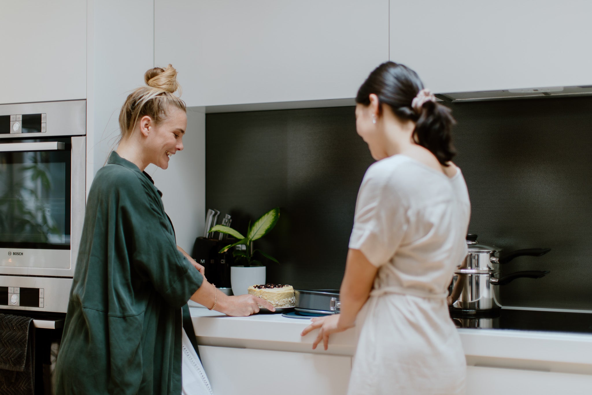 Two women smiling over a cake baked on a circular reusable cake tin liner