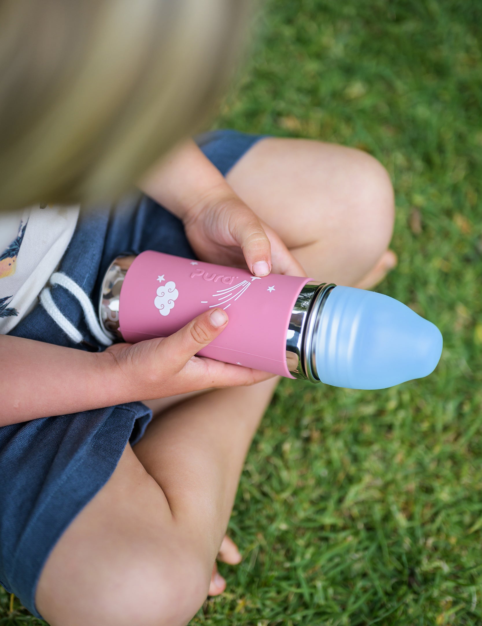 Pink pura water bottle held in the hands of a boy sitting cross legged 