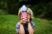 Boy holding pink unicorn CaliWoods stainless steel water bottle while sitting on the grass