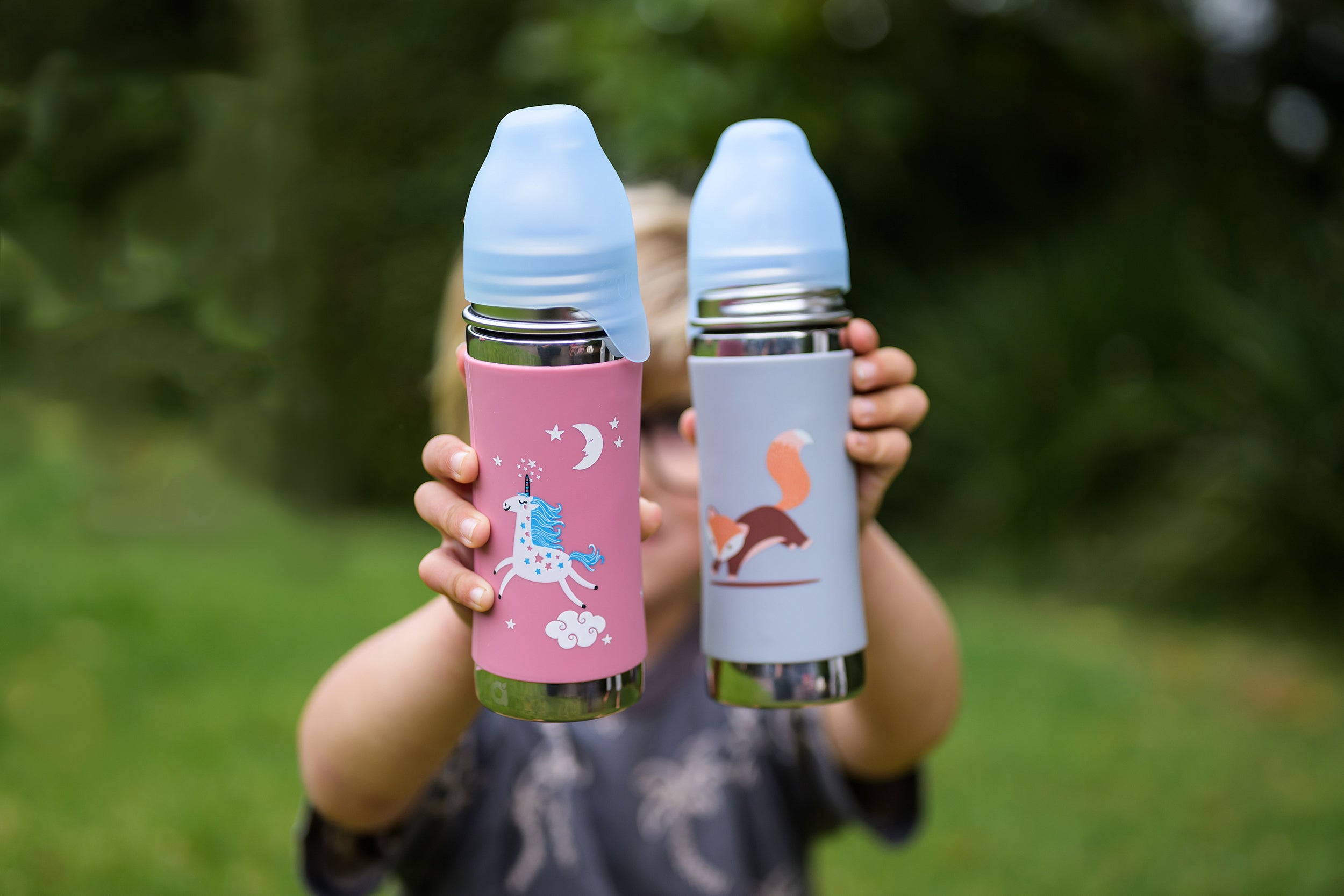 Pura Kiki water bottle in Unicorn and Fox being held out by small hands by a boy with the green background blurred