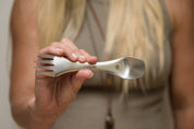 CaliWoods stainless steel spork being held by a woman who is in the background 