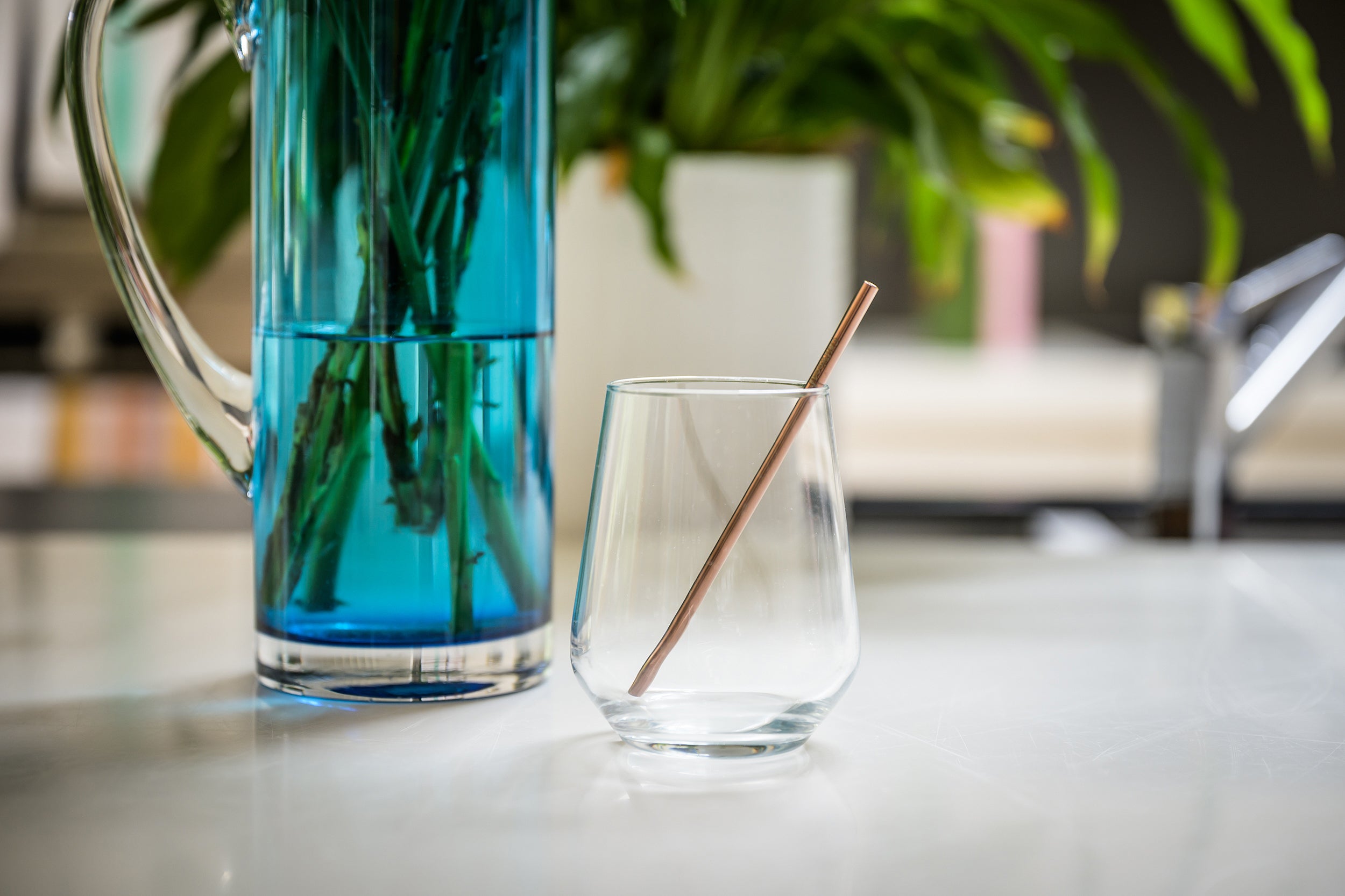 CaliWoods reusable short cocktail straw in rose gold sitting in a glass with a blue vase in the background 