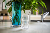 CaliWoods reusable stainless steel tall straw pack in a glass with a blue vase in the background