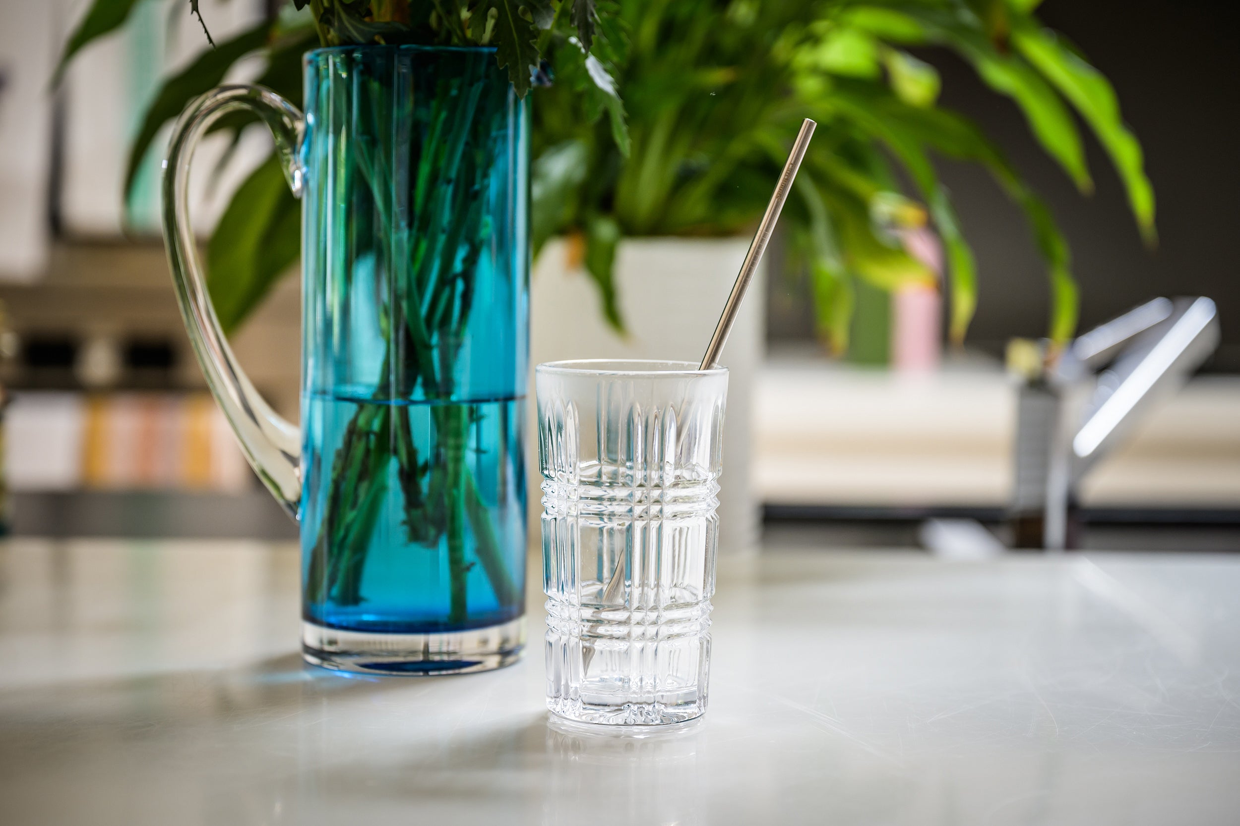 CaliWoods reusable stainless steel tall straw pack in a glass with a blue vase in the background